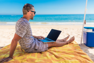 Young man relaxes on the beach under umbrella with laptop surf in internet.