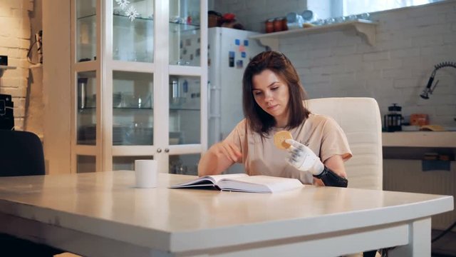 Young woman is reading a book and holding a cookie with her bionic hand