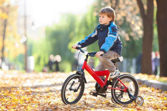 Happy boy with bicycle in the autumn park. Beauty nature scene with colorful foliage background, yellow trees and leaves at fall season. Autumn outdoor lifestyle. Boy  having fun on fall leaves