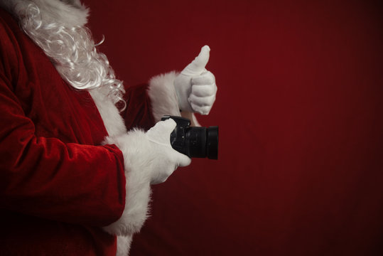 Santa Claus using DSLR camera taking images showing thumb up. Happy Christmas Evening and New Year celebration background. Fun loving creative costume time.