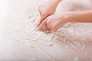 children's hands draw patterns of white flour on the table. baking preparation stage. little game