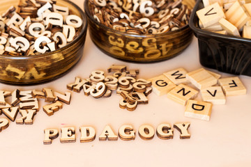 Word pedagogy made with  wooden letters next to a bowl of other letters and  numbers over pink background