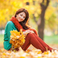 Young pretty woman relaxing in the autumn park. Beauty nature scene with colorful foliage background, yellow trees and leaves at fall season. Autumn outdoor lifestyle