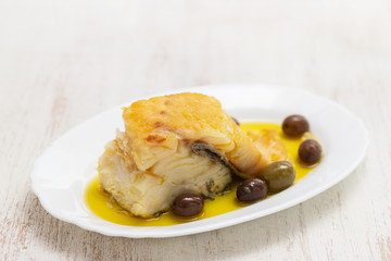 fried cod fish with olives and olive oil on white dish