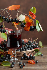 Fresh juice of ripe black chokeberry in glass and berries with leaves.