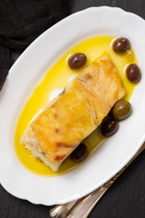 fried cod fish with olives and olive oil on white dish