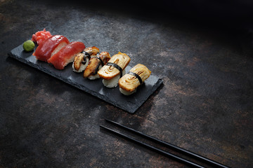 Nigiri na kamiennym talerzu. Apetyczne, różnorodne sushi na kamiennym talerzu. Kompozycja na ciemnym tle. - obrazy, fototapety, plakaty