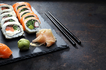 Sushi, rolki na ciemnym tle. Apetyczne, różnorodne sushi na kamiennym talerzu. Kompozycja na ciemnym tle.