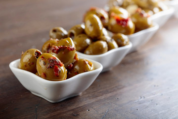 Spiced green olives in oil on a wooden table.