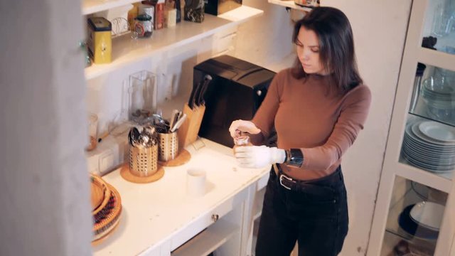 Young woman with a bionic hand adds spices into a coffee cup