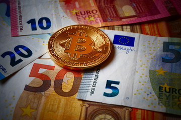 An golden Bitcoin, an virtual currency in physical coin form, displayed on Euro banknotes