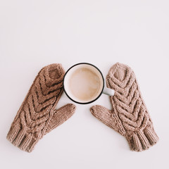 Warm knitted mittens with coffee cup isolated on white background. Flat lay, top view.