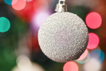 Christmas holiday decorations. White glitter ball on tree with fairy lights in background