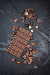 Top view of dark chocolate bar with cocoa beans and whole hazelnuts