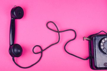 Black vintage phone and a receiver with a cord on a pink background, retro toned (minimal concept, top view)