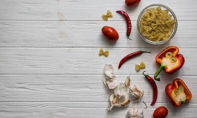 Ingredients. Pasta butterflies, red peppers, chilli peppers, garlic and tomatoes on a white wooden background. Top view. Copy space