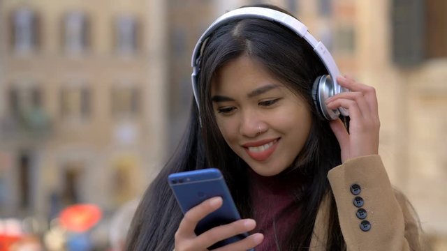 Beautiful asian woman with headphones and smartphone in the street,smiling 