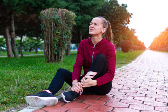 A young, fitness girl in sneakers and sportswear was injured while jogging and sports training. Leg injury and muscle strain, and ankle sprain accident during sports exercise.
