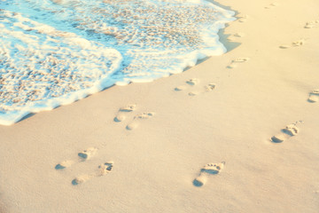 Footprints on a wet beach sand with sea water in sunny day