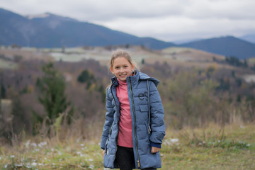 Fototapeta premium The child is smiling and happy against the backdrop of the mountains. Travel to the mountains. Girl happy in the mountains