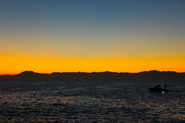 A small marine pleasure boat with tourists returns to port after sunset.