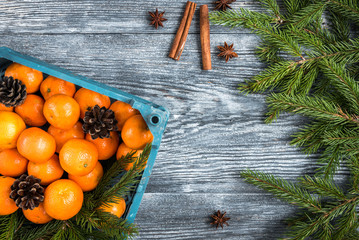 Mandarines on wooden background with Christmas fir branches, cinnamon sticks, anise stars and cones.
