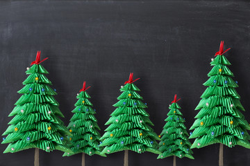 Origami Christmas trees from green paper on dark background or blackboard, with copy space