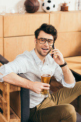 portrait of cheerful man with glass of beer in hand talking on smartphone in cafe