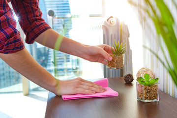 A housewife in a shirt is cleaning the house, wipes dust from the table with a cleaning rag....