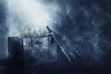 mysterious and magical image of old crown, wooden chest and sword over gothic black background....