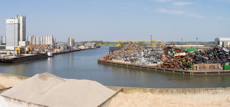 View over a canal in an industrial area near Kampen The Netherlands with factory buildings and old iron and scrap piles of sand warehouses
