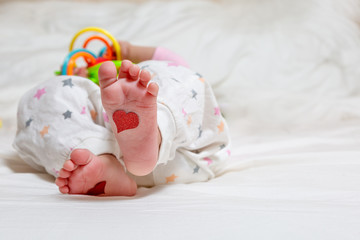 Fototapeta na wymiar Baby foots with hearts on their feet. A newborn baby is lying on the bed and play toys