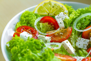 Fresh, healthy vegetable salad with feta cheese and lemon wedges in a plate. Healthy and right food. Diet