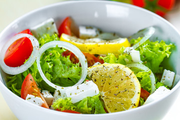 Fresh, healthy vegetable salad with feta cheese and lemon wedges in a plate. Healthy and right food. Diet