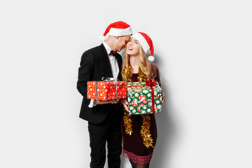 A happy couple of lovers, in Santa Claus hats, looking at each other, with Christmas gifts in their hands.