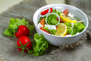 Fresh, healthy vegetable salad with lettuce, cherry tomatoes, onion, feta cheese, lemon, sprinkled with spices in a plate. Proper nutrition and right food. Diet