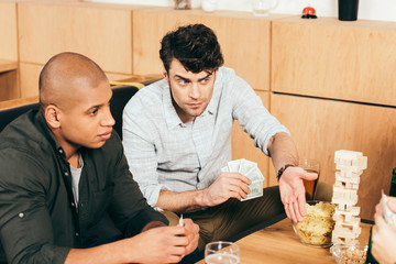 multicultural men playing cards while spending time together in cafe