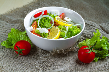 Fresh, healthy vegetable salad with lettuce, cherry tomatoes, onion, feta cheese, lemon, sprinkled with spices in a plate. Proper nutrition and right food. Diet