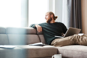 Concentrated young bearded man sitting in home using laptop computer.