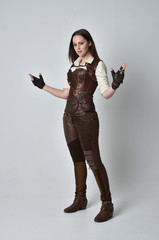 full length portrait of brunette  girl wearing brown leather steampunk outfit. standing pose on grey studio background.