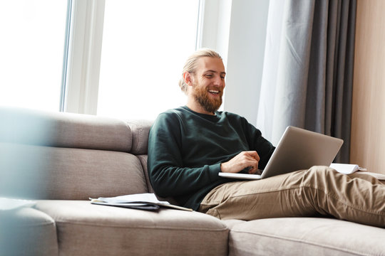 Concentrated young bearded man sitting in home using laptop computer.