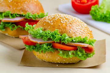 Appetizing sesame buns with fresh lettuce, tomato and ham for snack. Homemade sandwiches