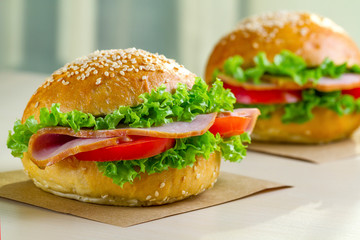 Appetizing sesame buns with fresh lettuce, tomato and ham for snack. Homemade sandwiches