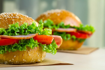 Appetizing sesame buns with fresh lettuce, tomato and ham for snack. Homemade sandwiches