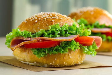 Appetizing sesame buns with fresh lettuce, tomato and ham for snack. Homemade sandwiches