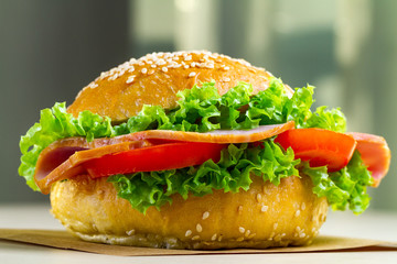 Appetizing sesame bun with fresh lettuce, tomato and ham for snack close up. Homemade sandwiches