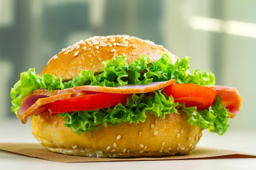 Appetizing sesame bun with fresh lettuce, tomato and ham for snack close up. Homemade sandwiches
