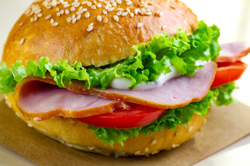 Appetizing sesame bun with fresh lettuce, tomato and ham for snack close up. Homemade sandwiches