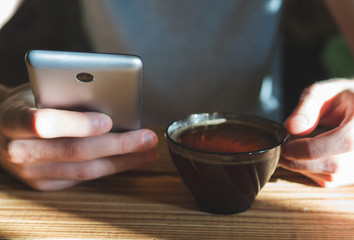 A man sits early in the morning in a cafe for a Cup of tea and uses a smartphone