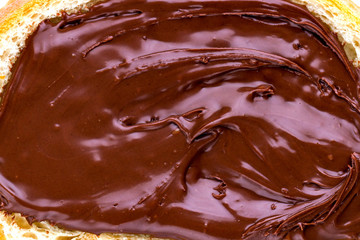 Piece of loaf with chocolate paste spread close up. Sandwich with nut paste on a breakfast. Chocolate texture